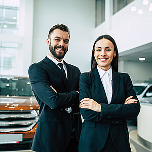 Zwei Autohändler stehen mit verschränkten Armen lächelnd in einem Autohaus